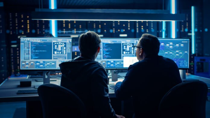 Two Professional IT Programers Discussing Blockchain Data Network Architecture Design and Development Shown on Desktop Computer Display. Working Data Center Technical Department with Server Racks